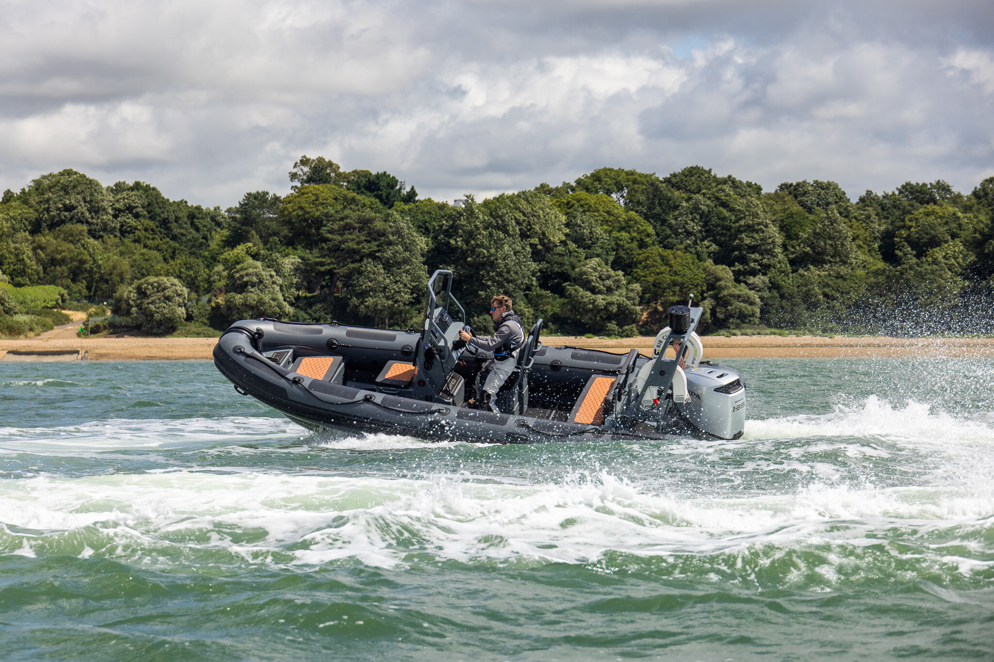 A RIB banking at speed near a wooded shore, throwing up spray.