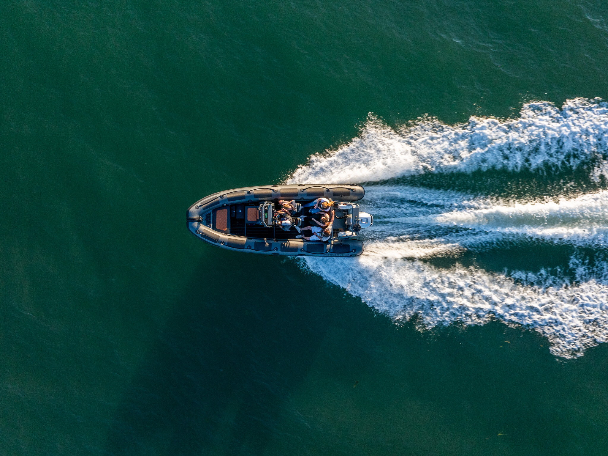A RIB seen from above, its white wake spreading across green water.