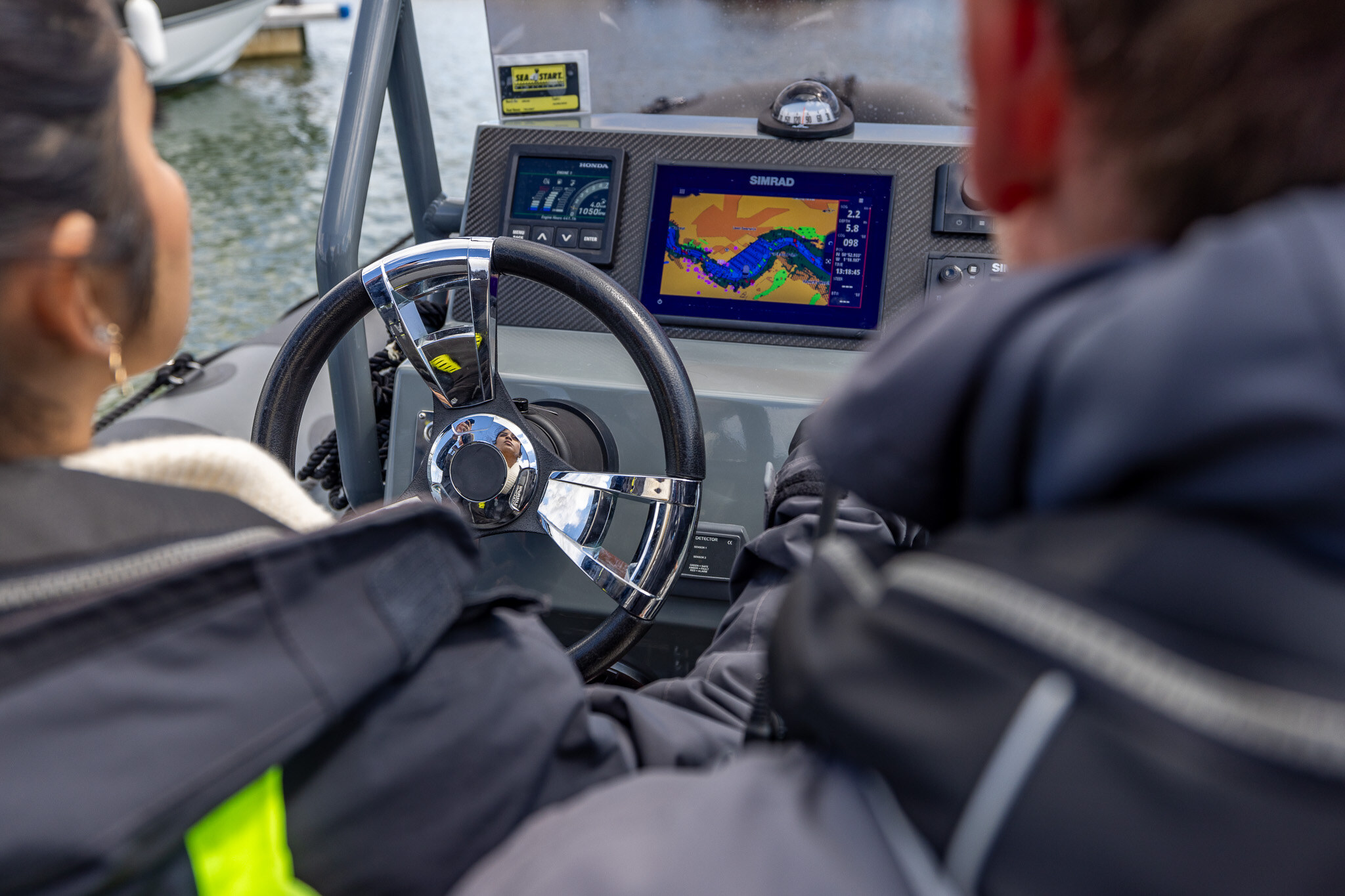 Over a student's shoulder: the RIB's wheel and chart plotter, her instructor beside her.