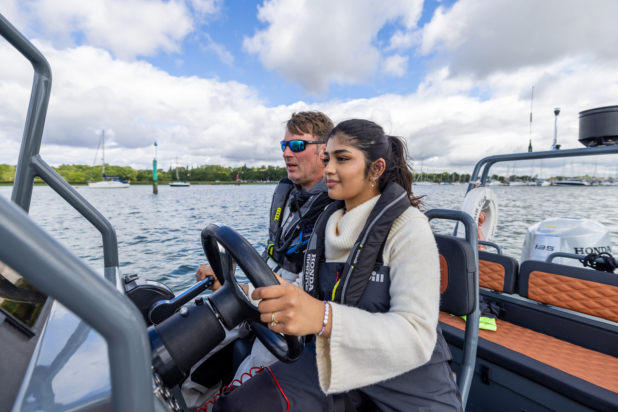 A student helms a RIB across a harbour, her instructor beside her.