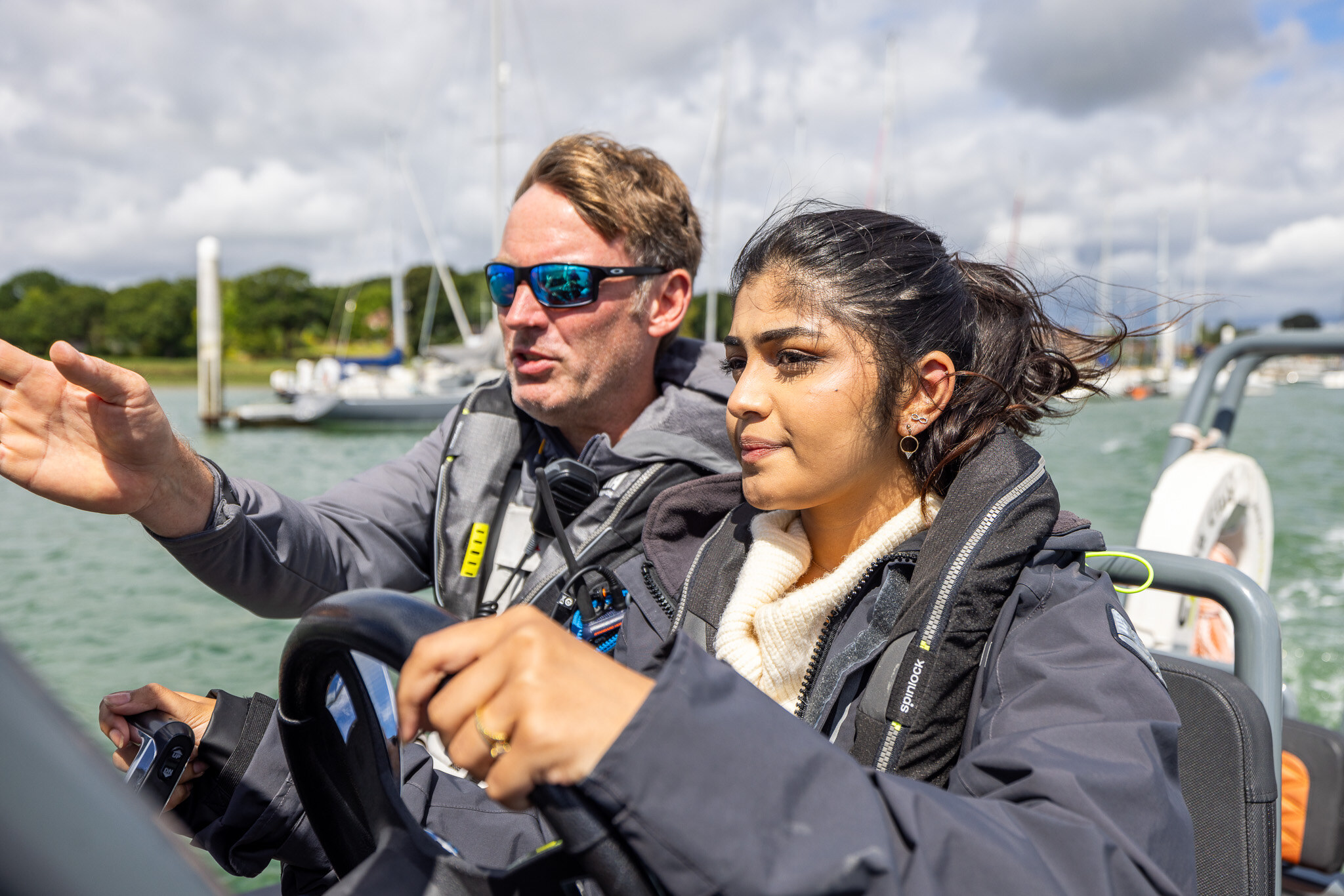An instructor points out a mark while the student at the helm looks ahead.