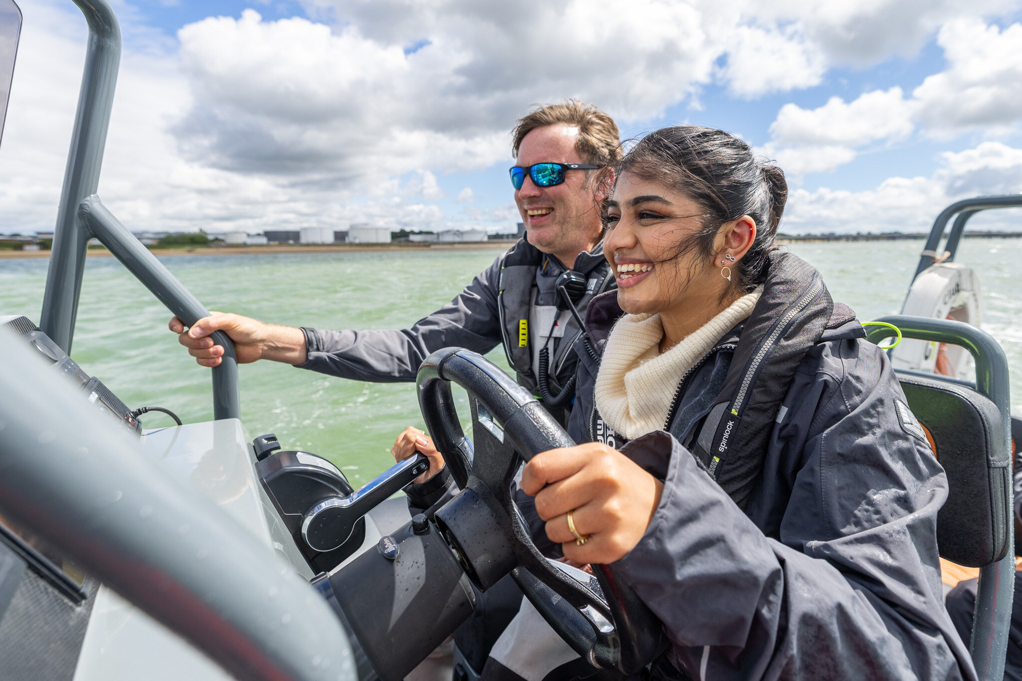 A student laughs at the helm of a RIB, her instructor smiling behind her.